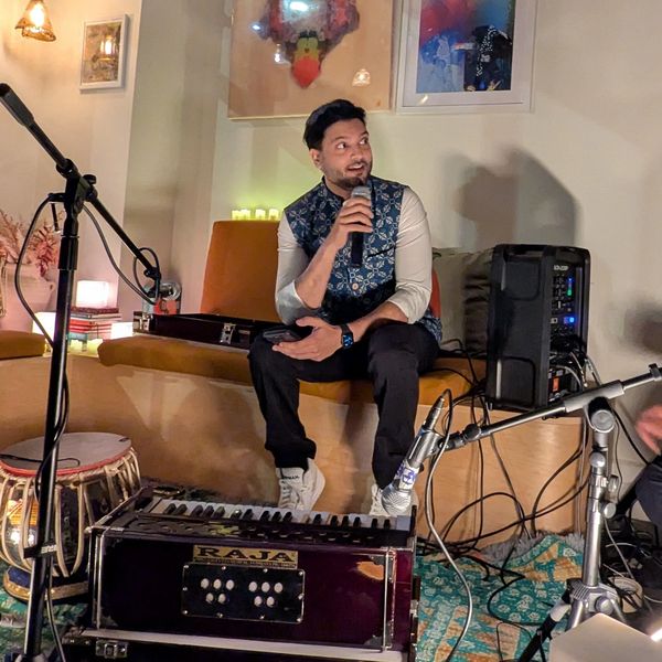 A man holding a microphone sits with musical instruments around him.
