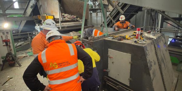 Workers in safety gear inspecting industrial machinery indoors.