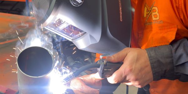 A person welding a metal pipe while wearing protective gear.