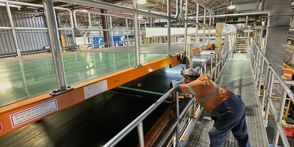 Worker inspecting equipment on an elevated platform in a factory.