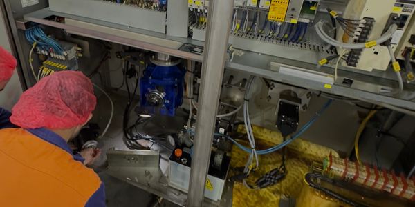 Worker in a red hairnet operates machinery in a factory setting.