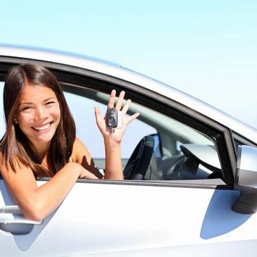 Smiling woman holding car keys inside a white car.