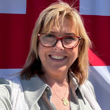 Smiling woman with glasses in front of a red and white flag.