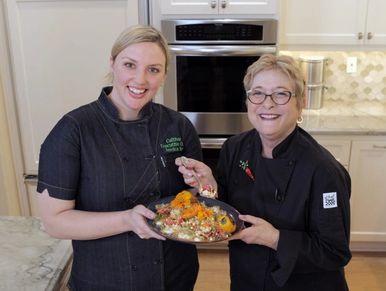 Chef Jessica Roy with Cathy Thomas smiling and holding a plate of grilled corn salad 