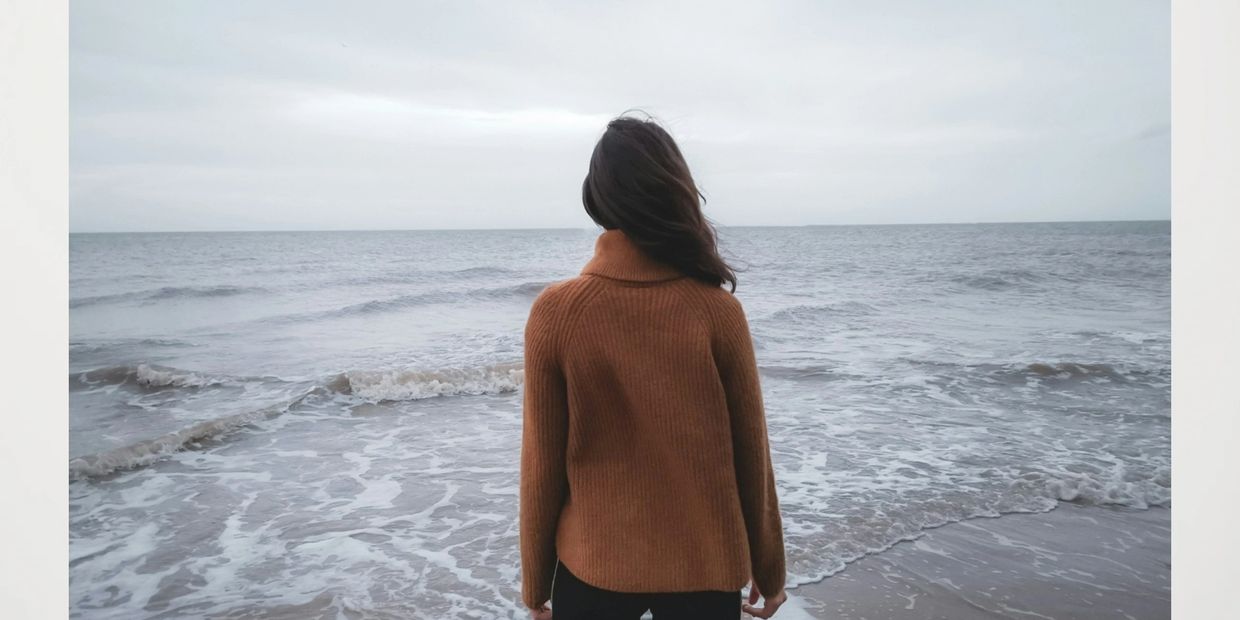 Person in brown sweater looking at the ocean.