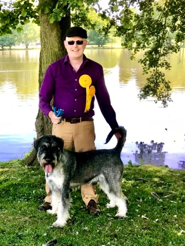 Man in purple shirt with dog by a lake, holding ribbons.