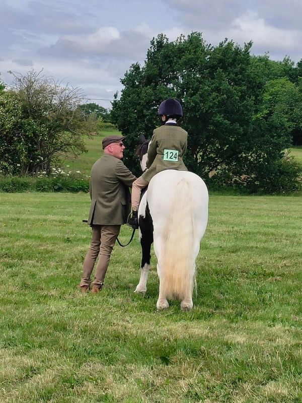 A child on a horse with a man standing beside them in a grassy field.