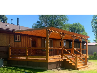 Wooden deck with pergola attached to a rustic house under clear blue sky.