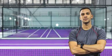 Man standing confidently on an indoor purple tennis court.