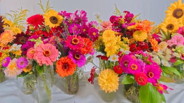 Colorful mixed flower bouquets arranged in glass vases on a white surface.