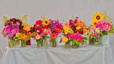 Colorful flower bouquets arranged in various glass jars on a white cloth-covered table.
