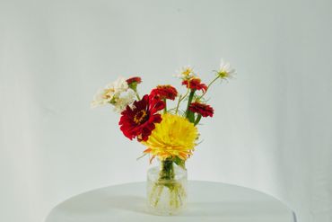 A vibrant bouquet of red, yellow, and white flowers in a clear vase on a white table.