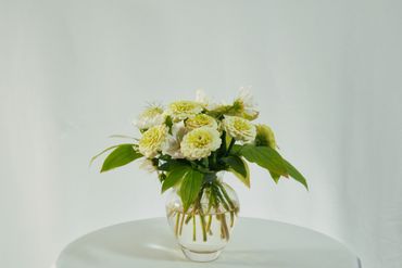 A delicate bouquet of pale yellow and white flowers in a clear glass vase.
