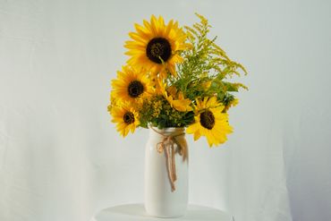 Bright sunflowers arranged in a white vase with a rustic twine bow.
