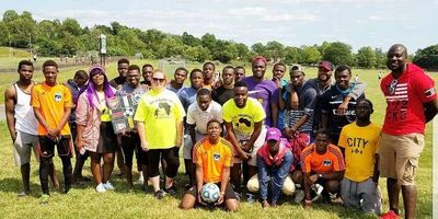 Group of people posing on a grassy field with a soccer ball.
