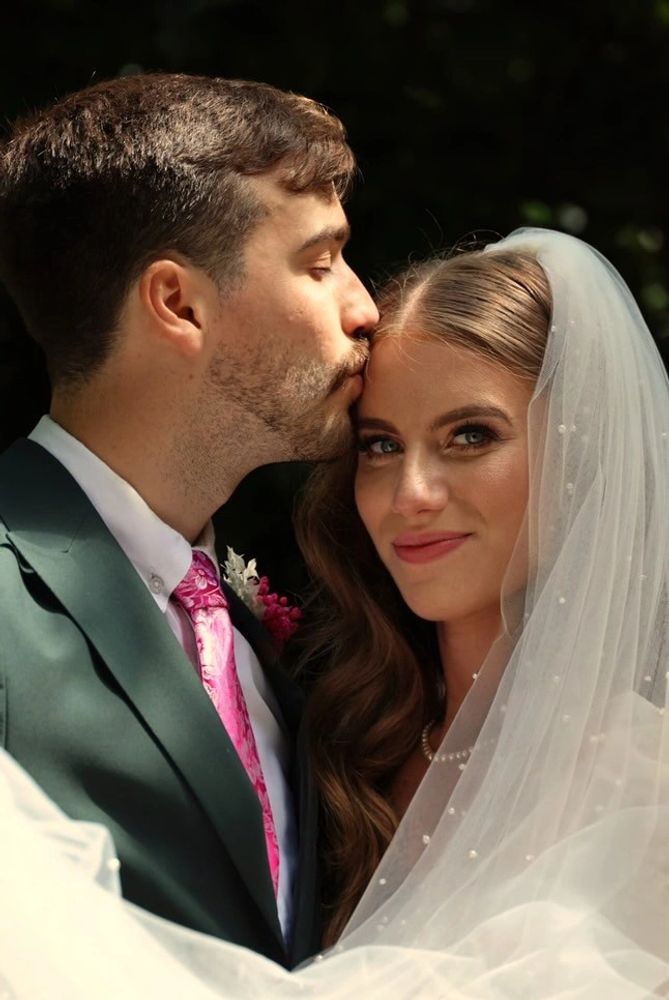 Groom kissing bride's forehead during wedding, bride smiling with veil.