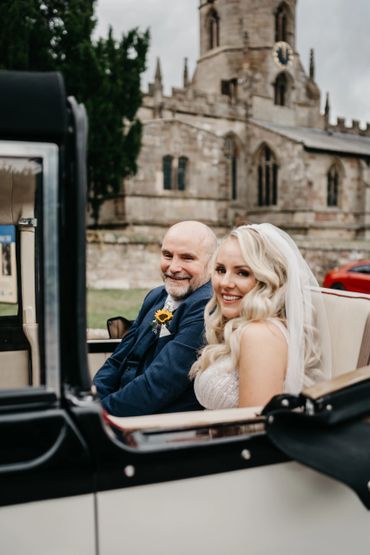 Happy bride and groom sitting in a vintage car outside a church.
