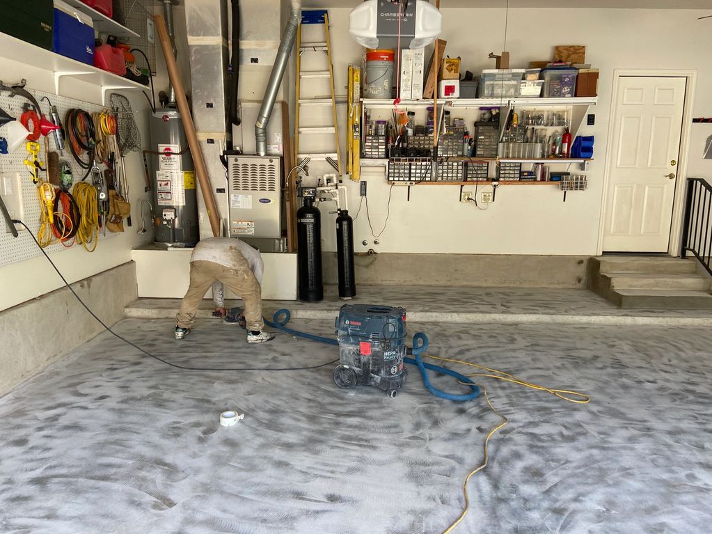 Person working on a garage floor with tools and equipment.
