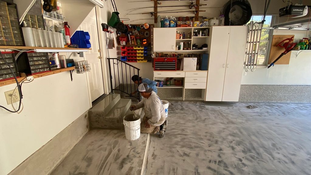 Two workers smoothing concrete stairs in a garage.
