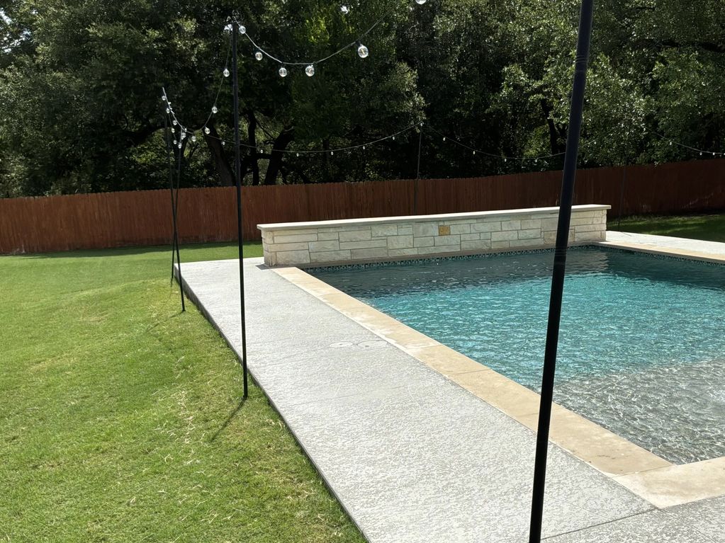 Outdoor swimming pool with stone tiles and string lights.