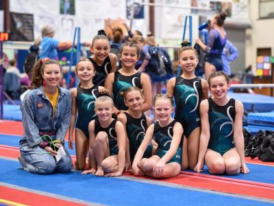 Group of young gymnasts posing with their coach on a gym floor.