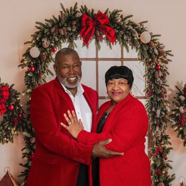 Smiling couple in red outfits posing before a festive holiday wreath.