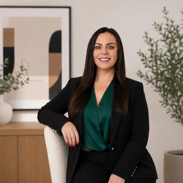 Confident woman in a black blazer and green blouse smiling while seated in a modern office.