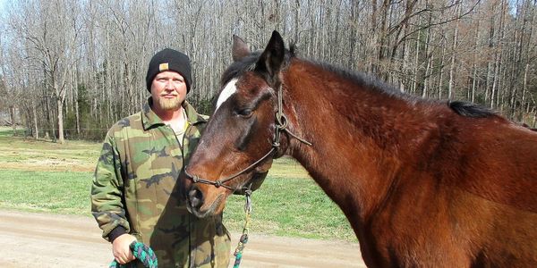 A man wearing camoflauge holding a brown/bay horse