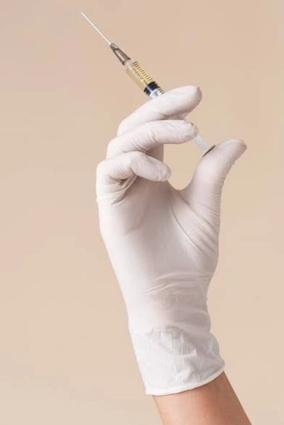 Hand in a white glove holding a syringe with liquid.