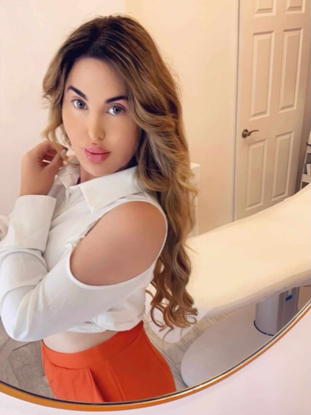 Woman in white top with open shoulder and orange pants.