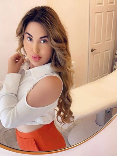 Woman in white top with open shoulder and orange pants.
