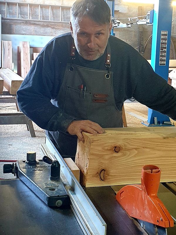 A man working with wood on a table saw in a workshop.