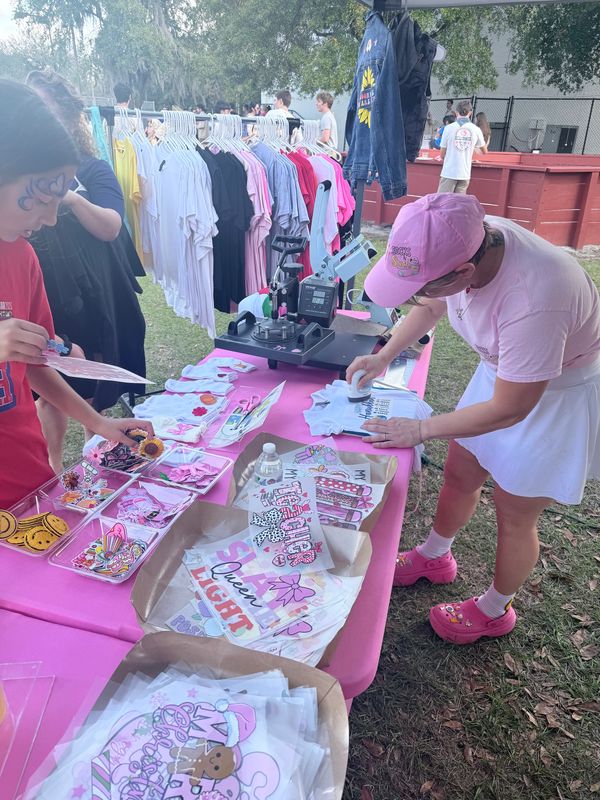People browsing a colorful outdoor market stall with shirts and accessories.