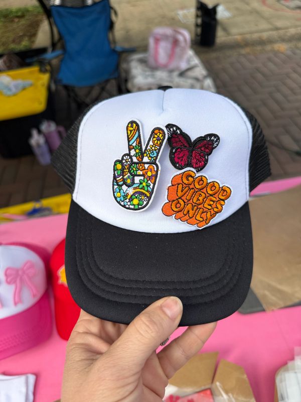 A colorful trucker hat with peace sign, butterfly, and 'Good Vibes Only' patches.