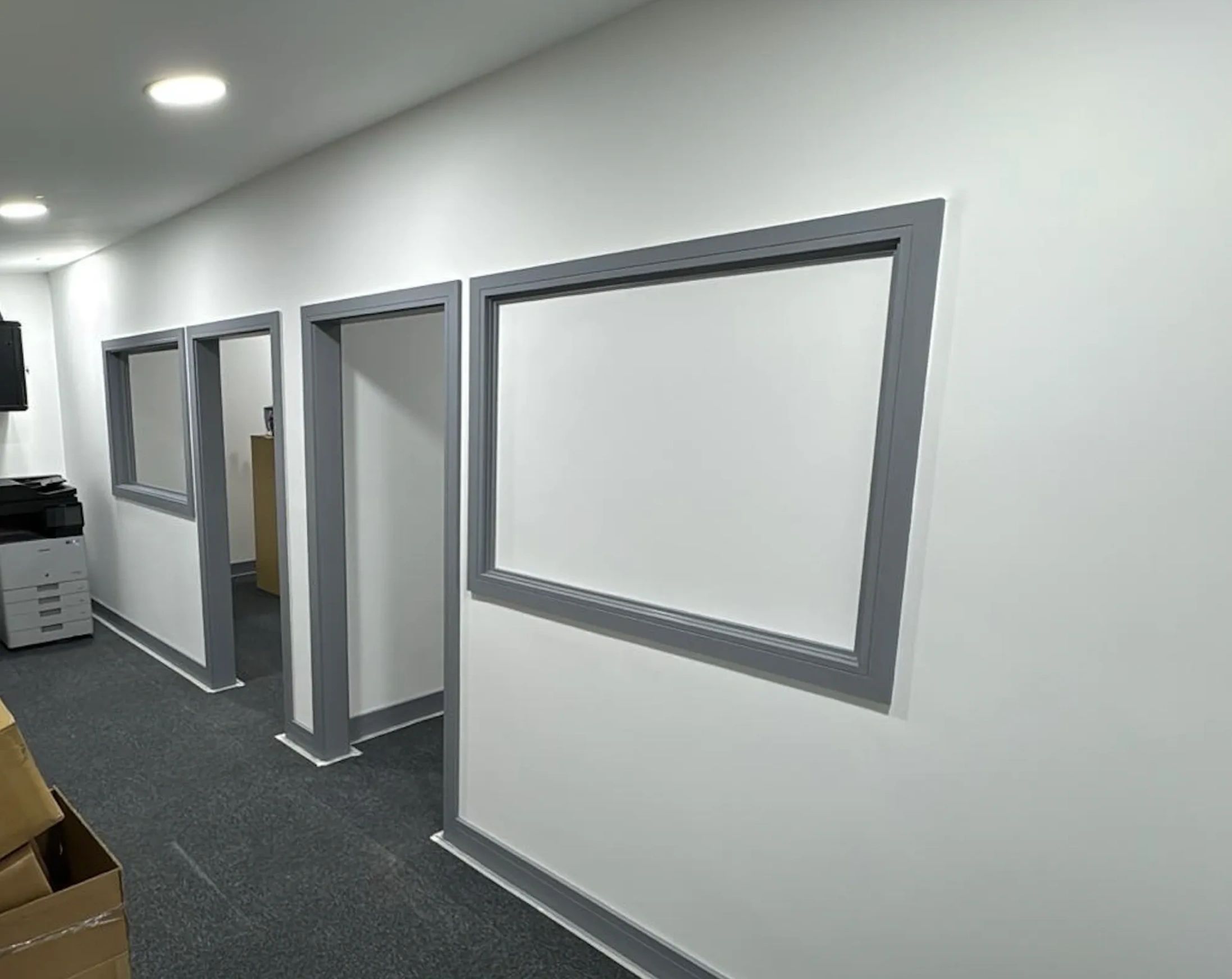 Office hallway with grey-framed openings and white walls.