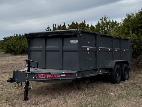 A large black dump trailer parked on grassy land under a cloudy sky.