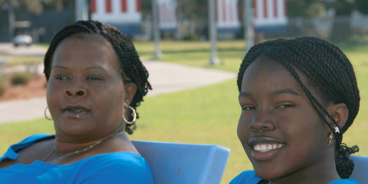 Two women with braided hair sitting outdoors on blue chairs.