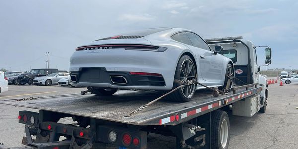 Silver Porsche 911 Carrera on a flatbed tow truck in a parking lot. car hauling services
door-to-door transport
vehicle shipping