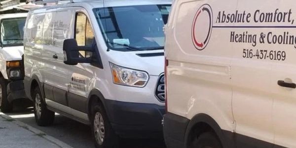 Two white vans parked on a street, one with HVAC service signage.