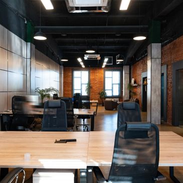 Modern office space with desks, chairs, and natural light from large windows.