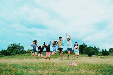 Group of friends joyfully jumping in a grassy field under a cloudy sky.