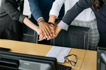 Colleagues joining hands in teamwork over an office desk.