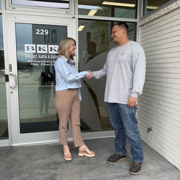 Two people shaking hands outside an office entrance with company signage.