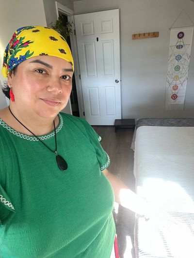Woman in a green shirt and yellow headscarf smiling indoors.