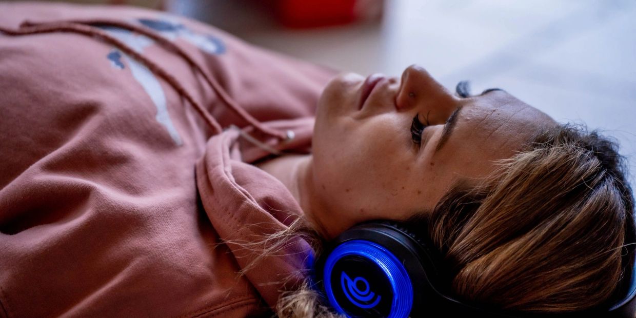 Person lying down wearing a pink hoodie and blue glowing headphones.