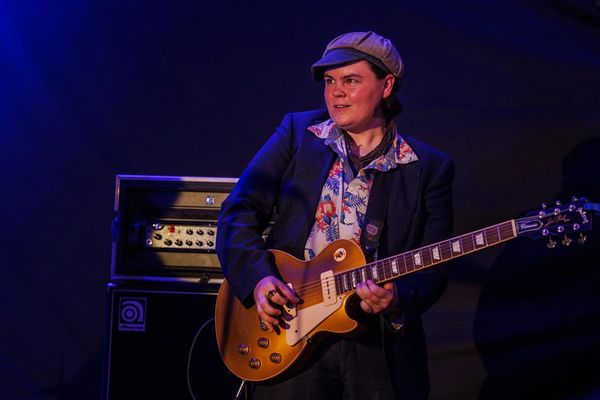 Musician playing an electric guitar on stage with focused expression.
