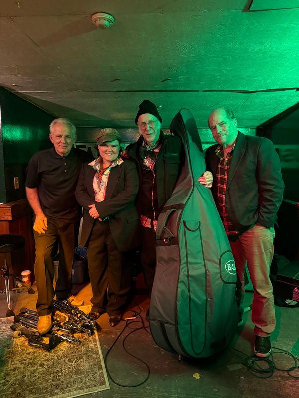 Four people posing together in a music studio with instruments around.