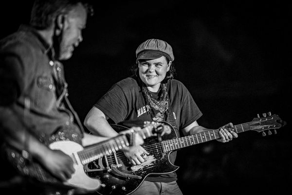 Two musicians playing electric guitars, sharing a joyful moment on stage.
