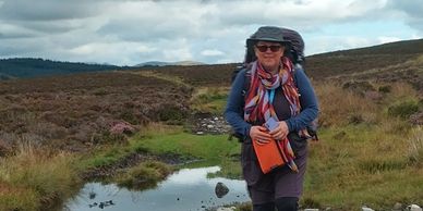 Hiker walking on a rugged trail under cloudy skies in a moorland.
