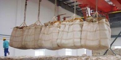 Large sacks suspended by crane inside a warehouse.
